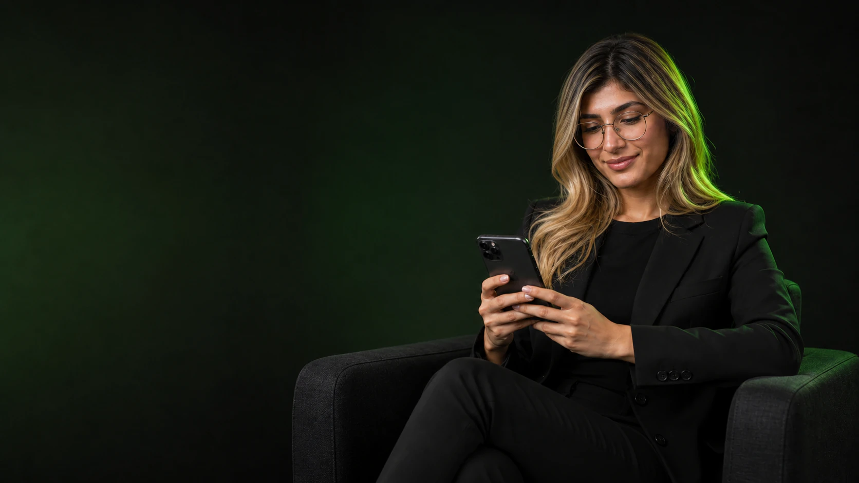 A blonde woman with glasses looking at her phone while seated in a lounge chair